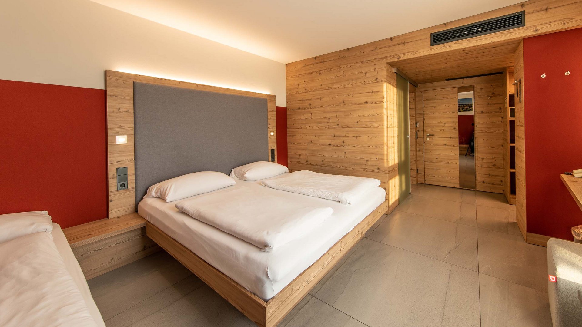 Modern hotel room with wood paneling, double bed, and red accent wall