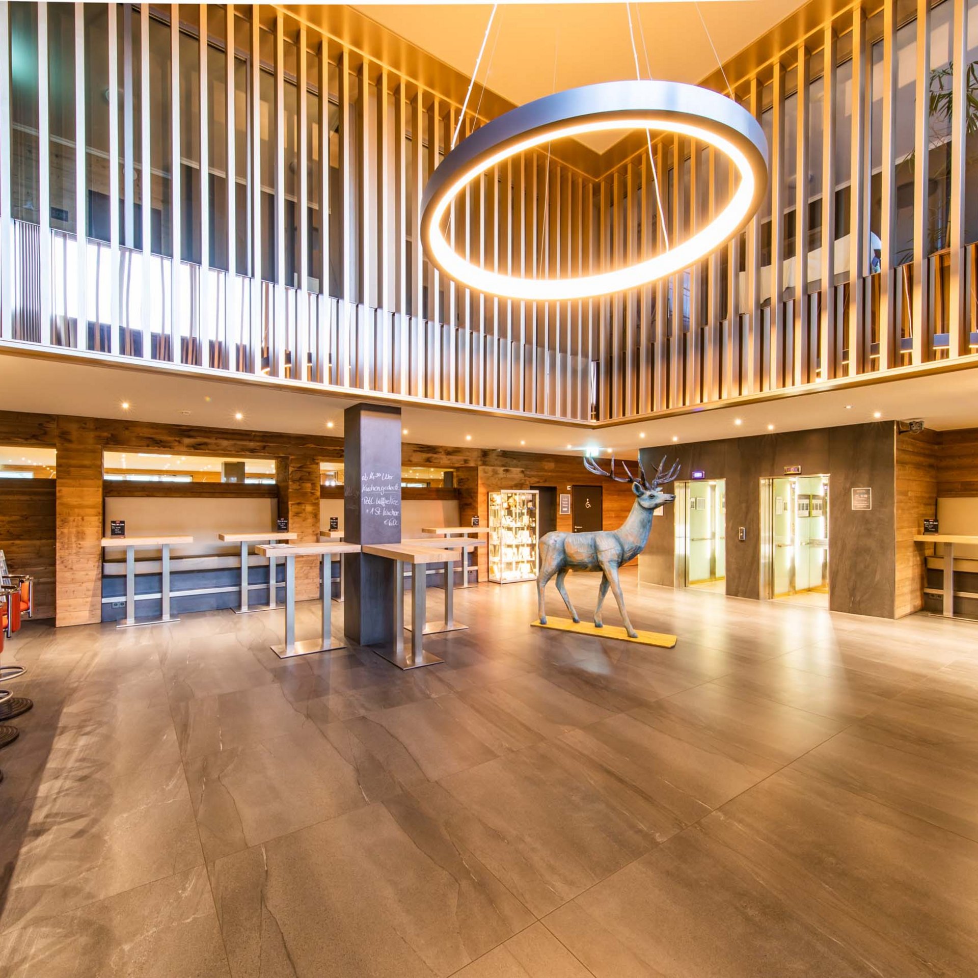 Helle Hotellobby mit modernem Kronleuchter und Hirschskulptur in der Mitte