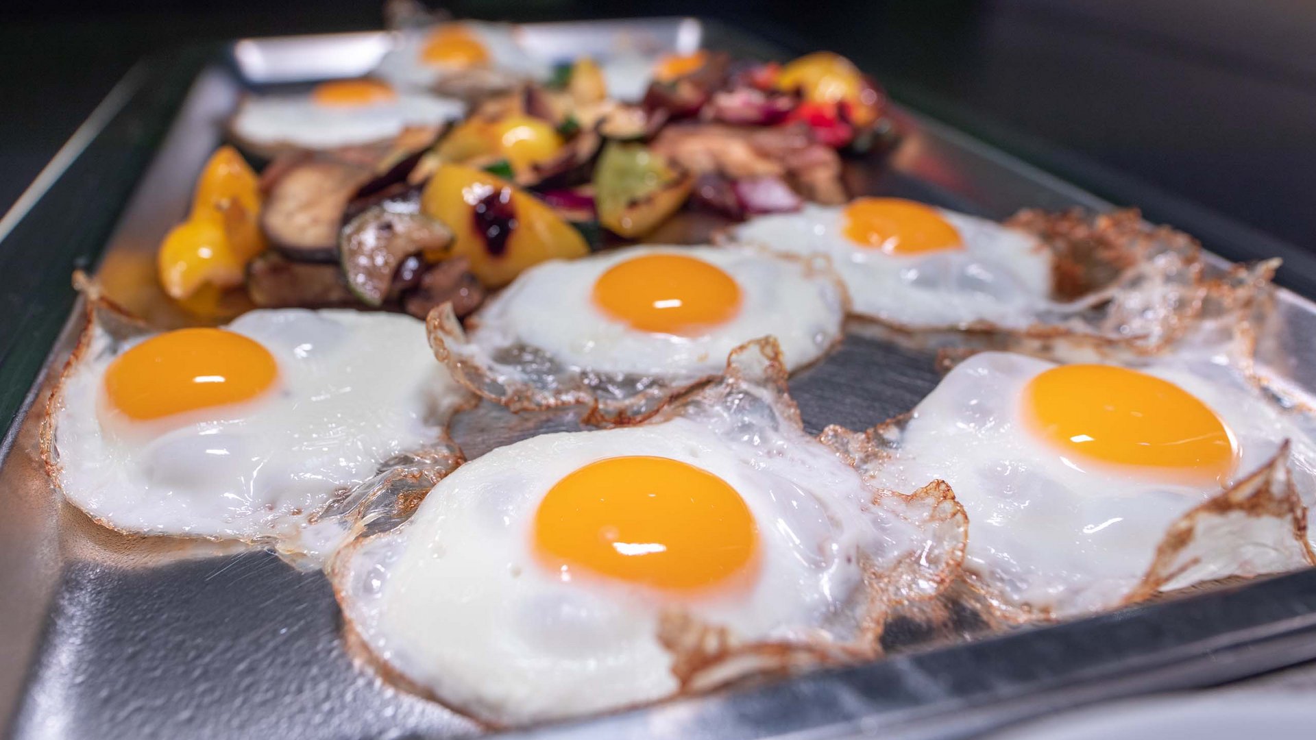 Fried eggs and sautéed vegetables on a metal tray