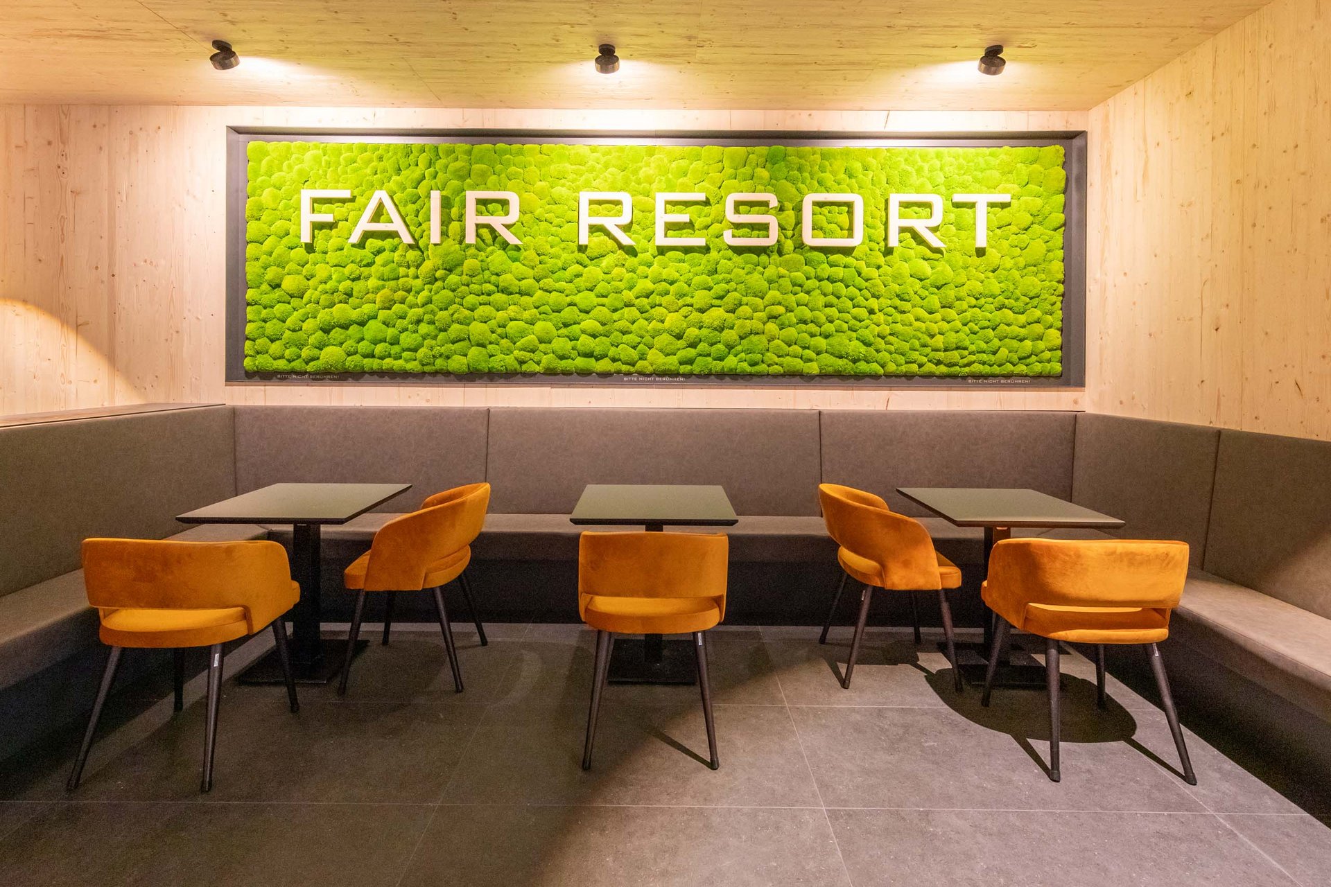 Moderner Sitzbereich mit orangefarbenen Stühlen und grünem FAIR RESORT Schriftzug an der Wand