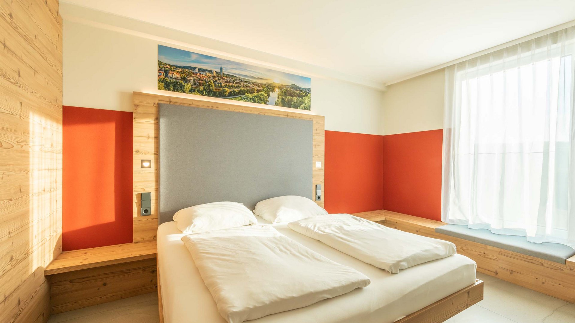 Modern bedroom with double bed, wood paneling, and large window with curtain