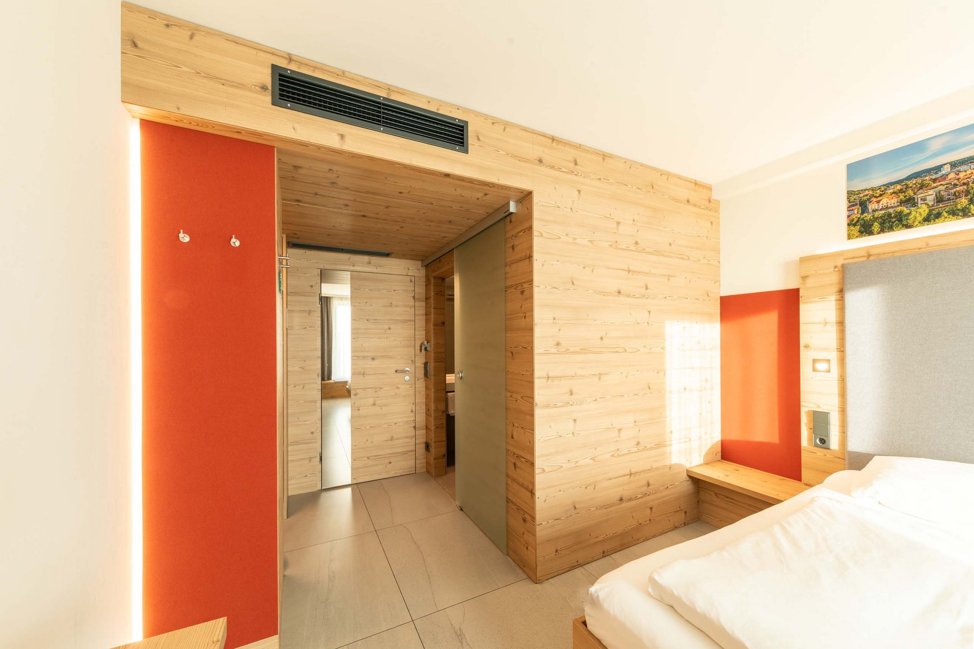 Helles Hotelzimmer mit Holzwänden, rotem Akzent und weißem Bett