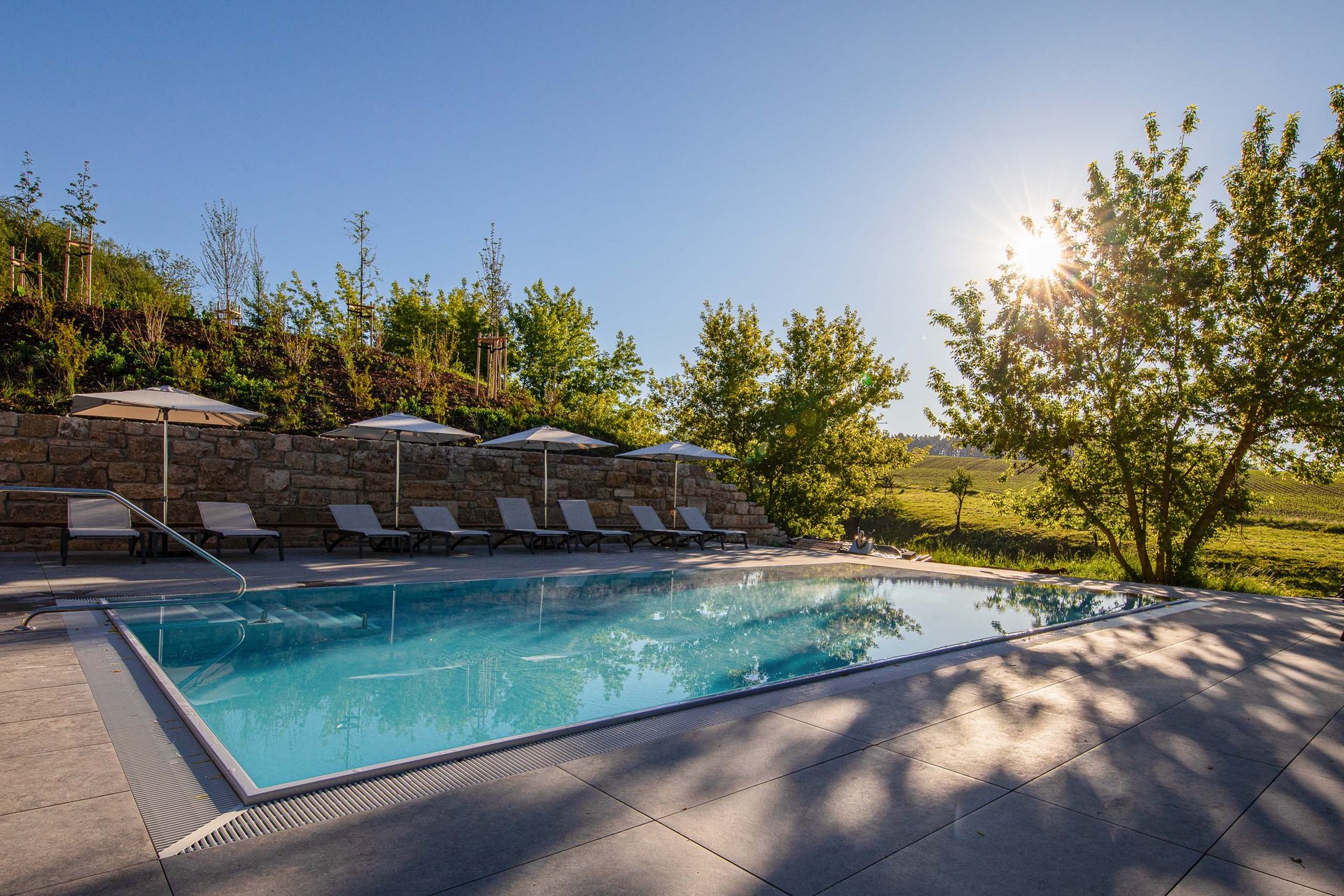 Freizeitpool mit Liegestühlen und Sonnenschirmen in sonniger ländlicher Umgebung