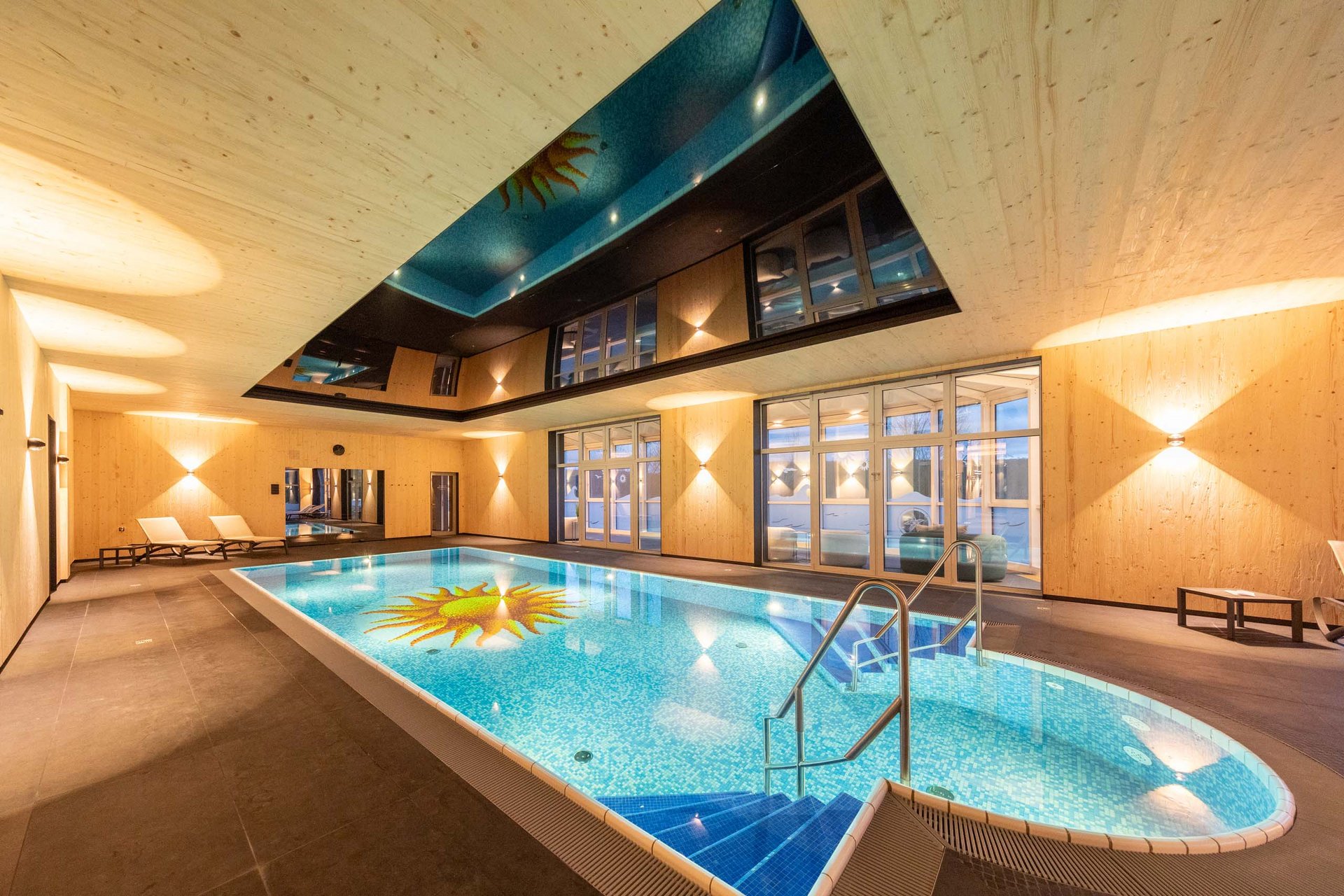 Innenpool mit Holzverkleidung, Lounge-Stühlen und beleuchtetem Schwimmbecken