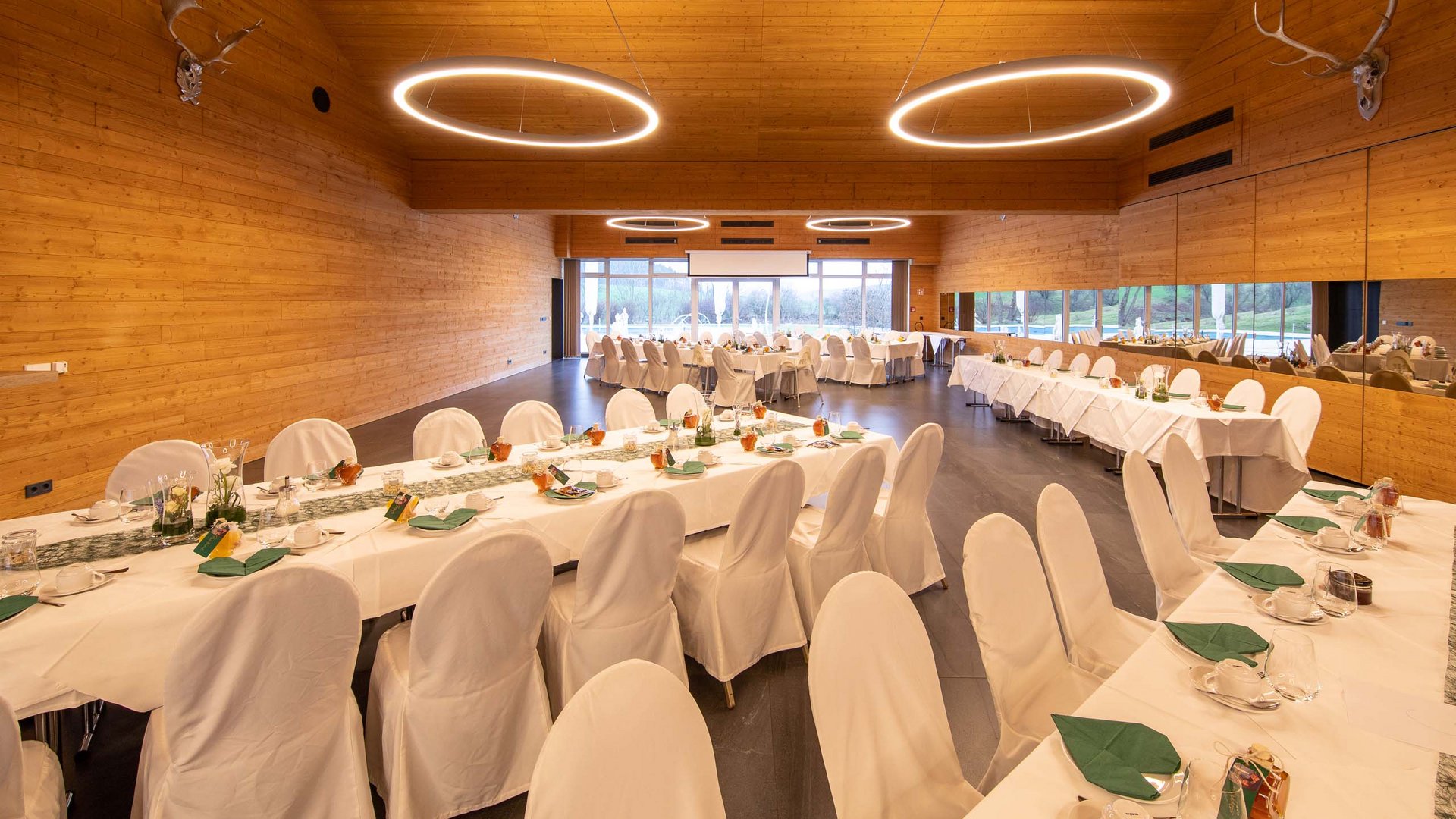 Festively set tables in a large, modern event room with wooden paneling