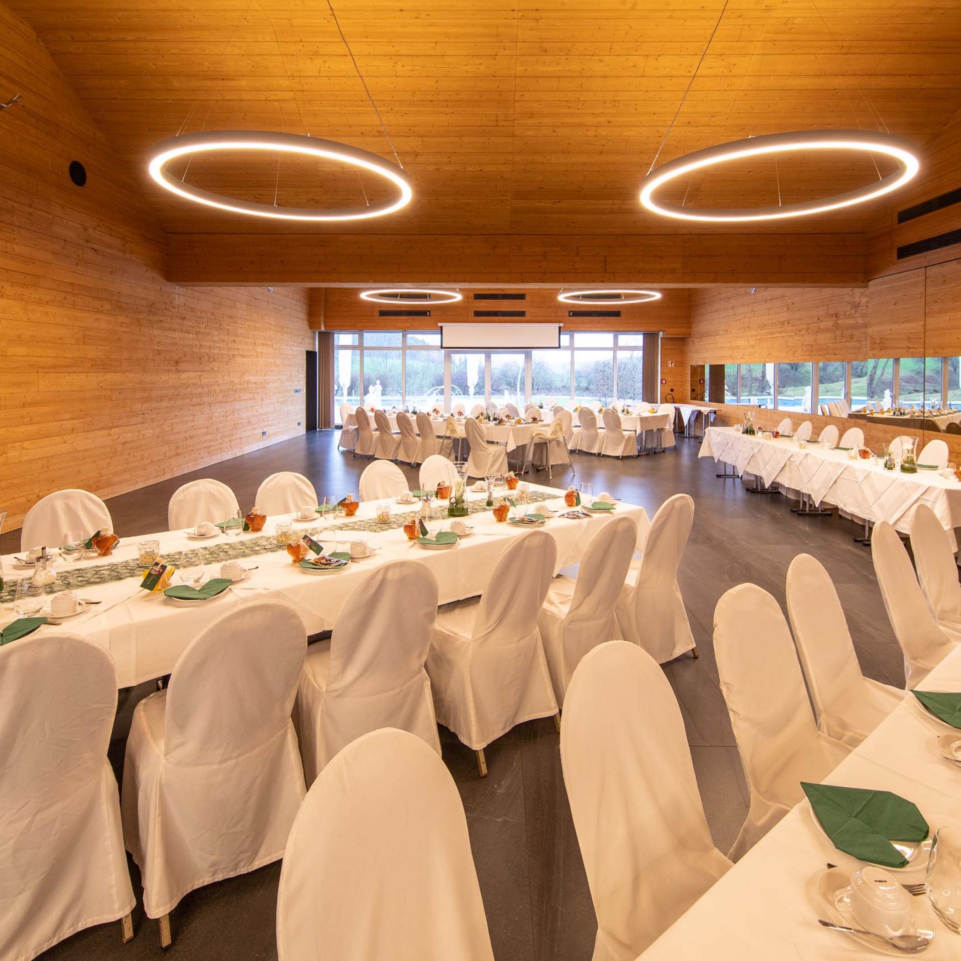Festively set tables in a large, modern event room with wooden paneling
