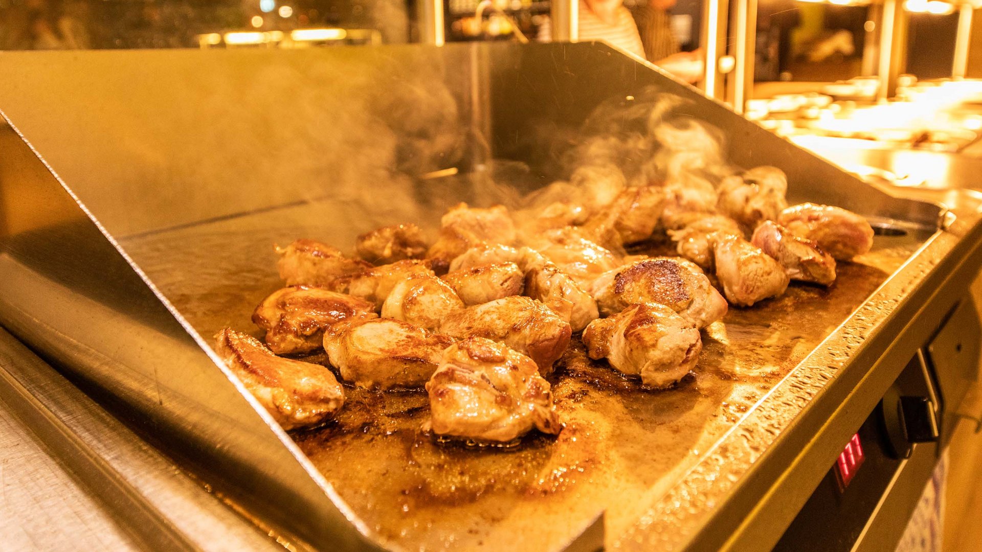 Chicken pieces cooking on a hot griddle with steam rising