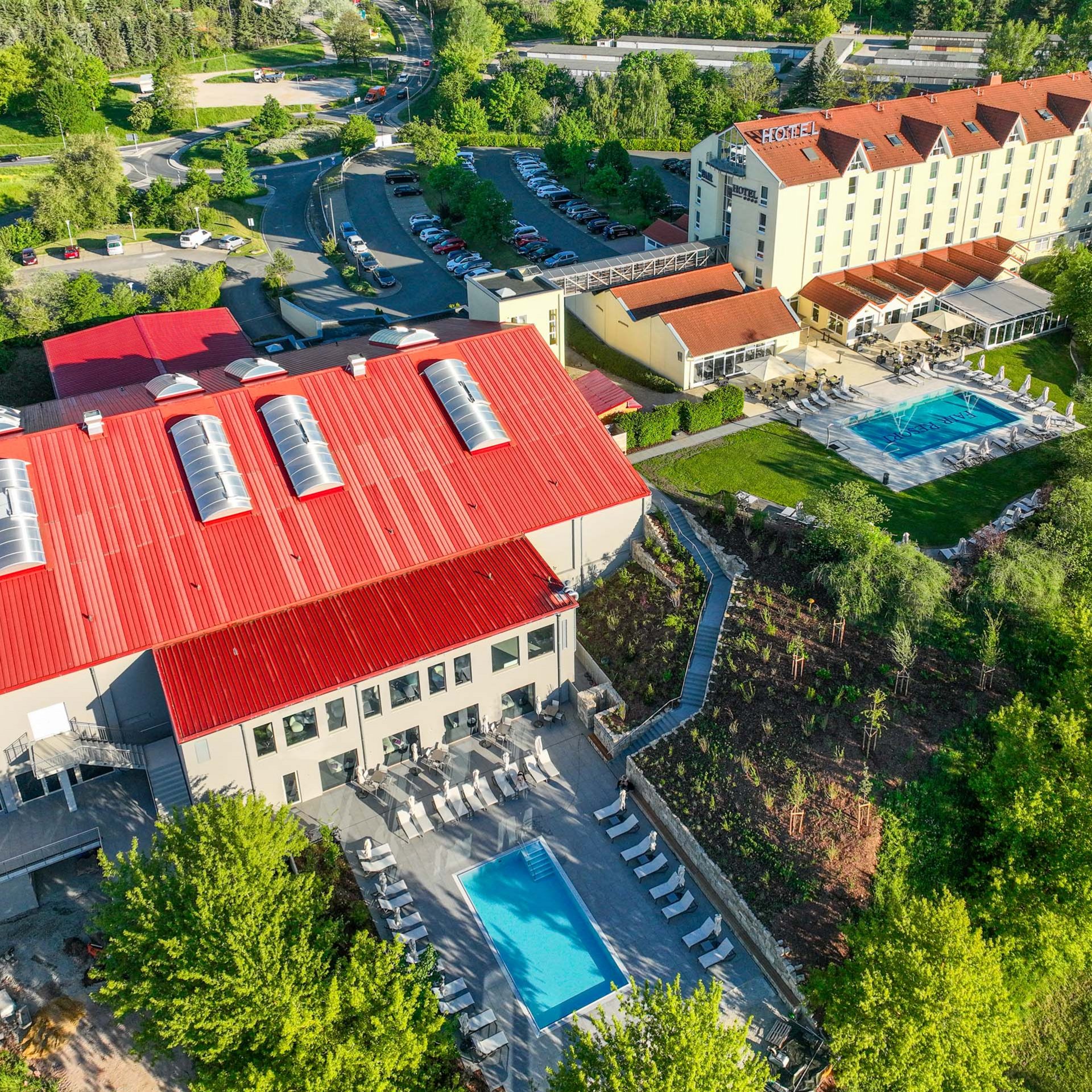 Luftaufnahme eines Hotels mit rotem Dach, zwei Swimmingpools und viel Grün