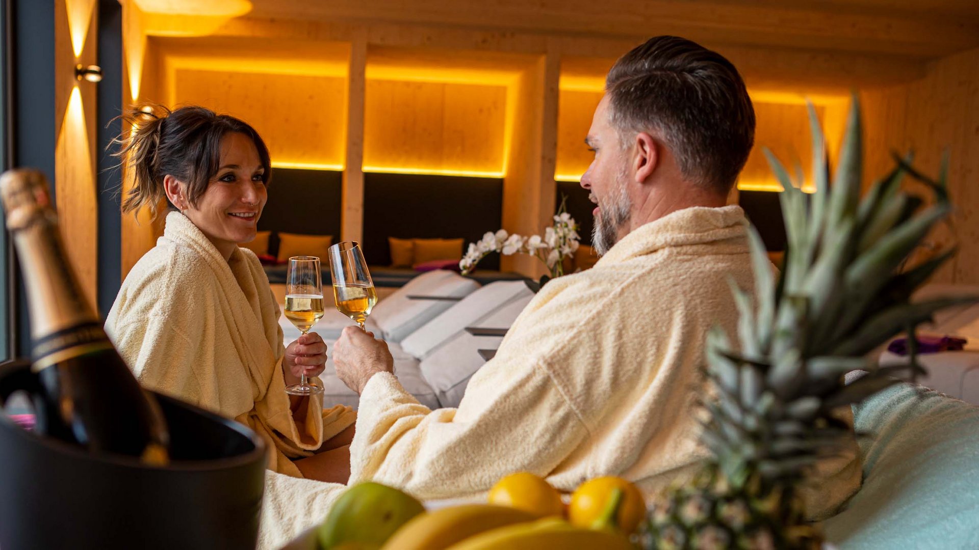 Couple in bathrobes toasting with champagne glasses in a cozy spa setting