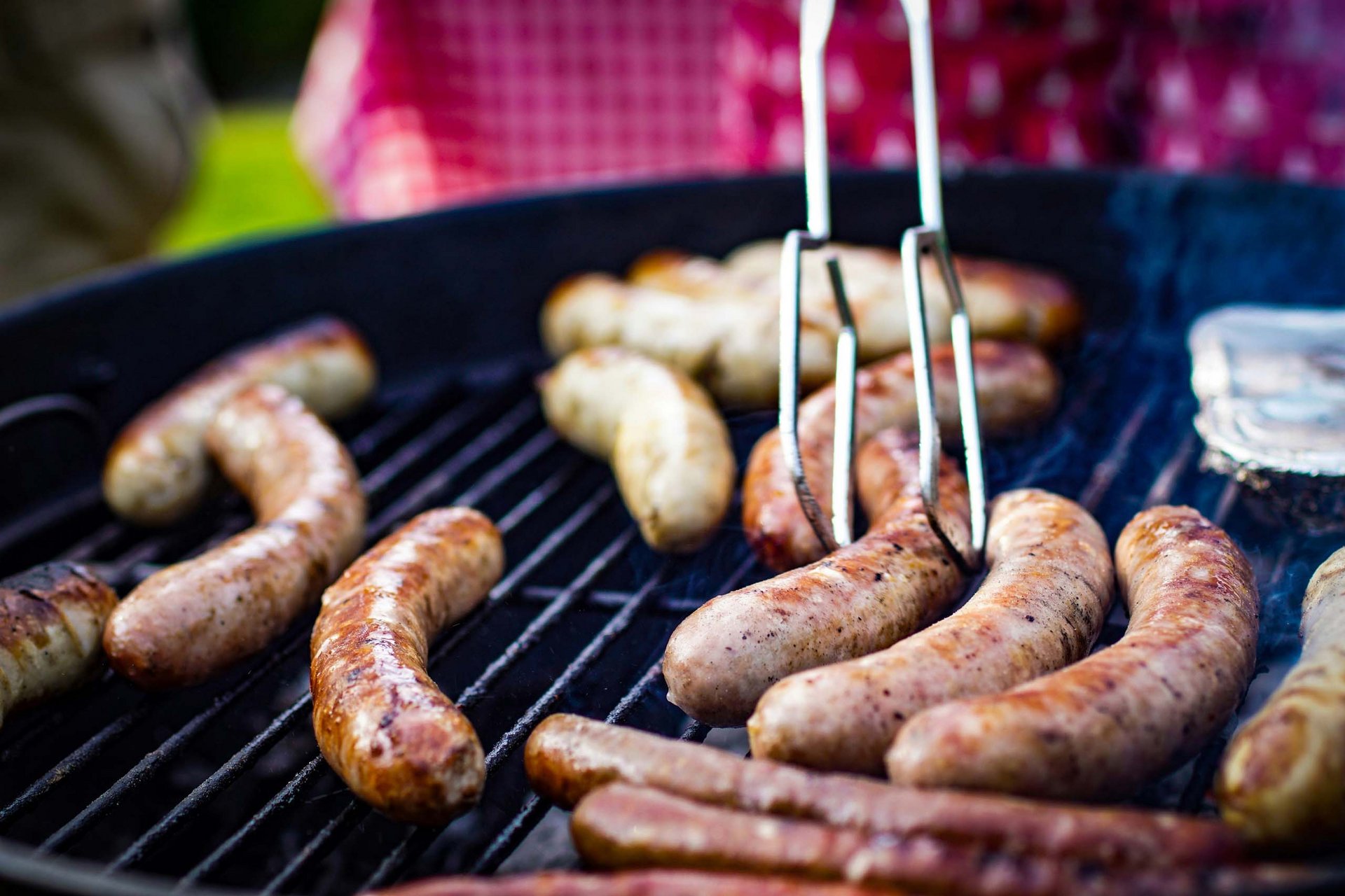 Bratwürste werden auf einem Grill im Freien mit Grillzange gewendet