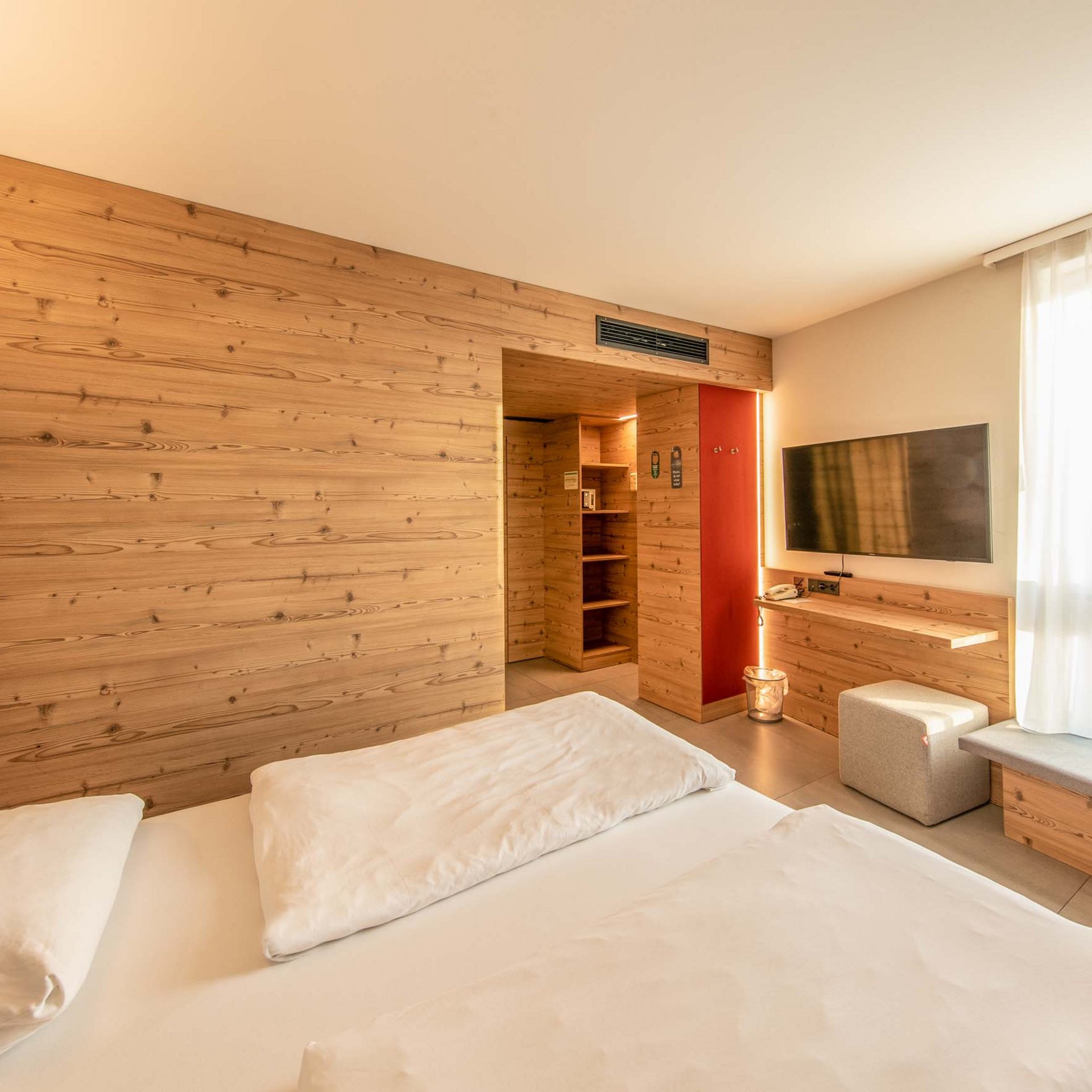 Helles Hotelzimmer mit Doppelbett, TV und Holzwandgestaltung