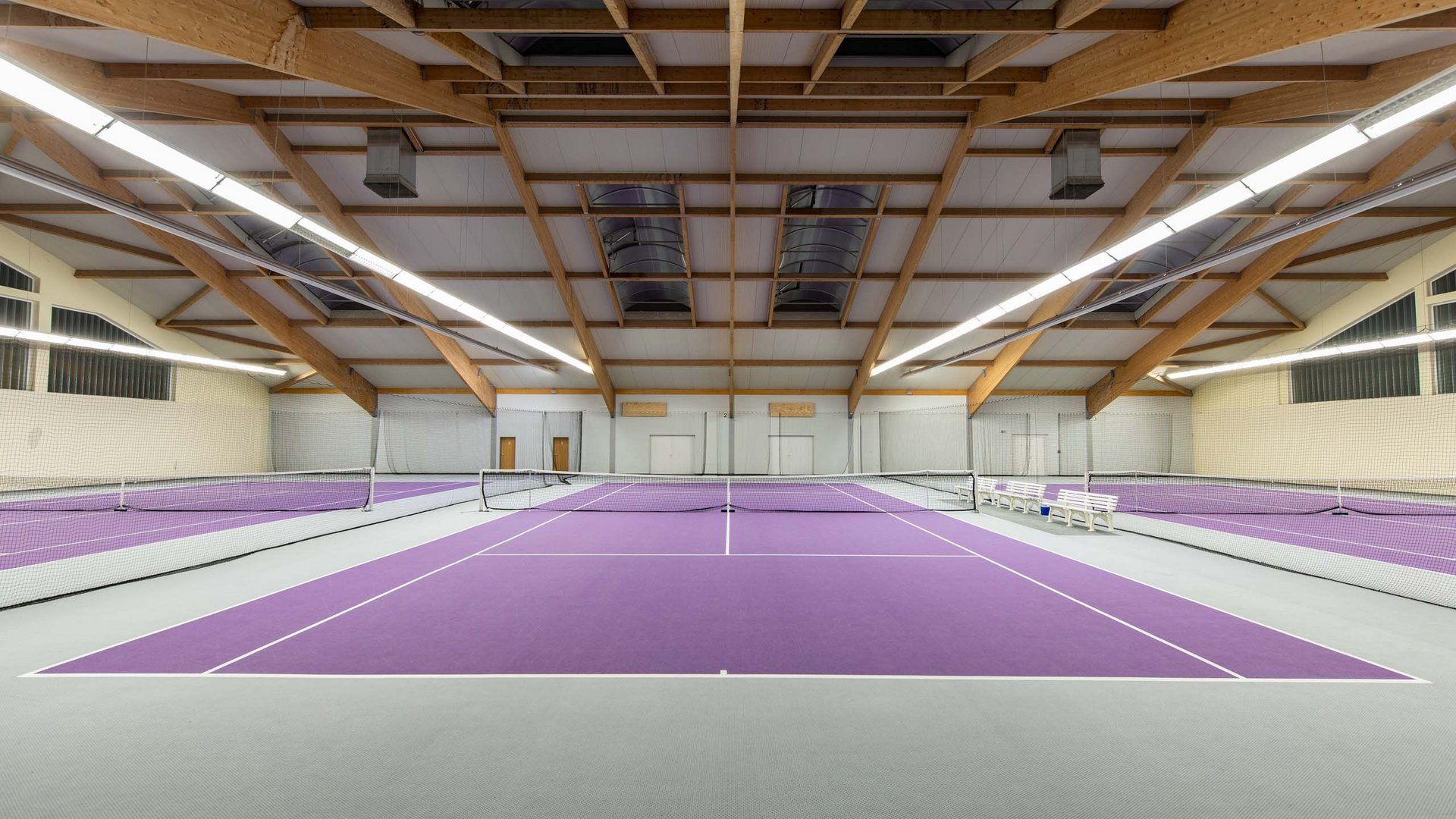 Empty indoor tennis court with purple surface and wooden beam ceiling
