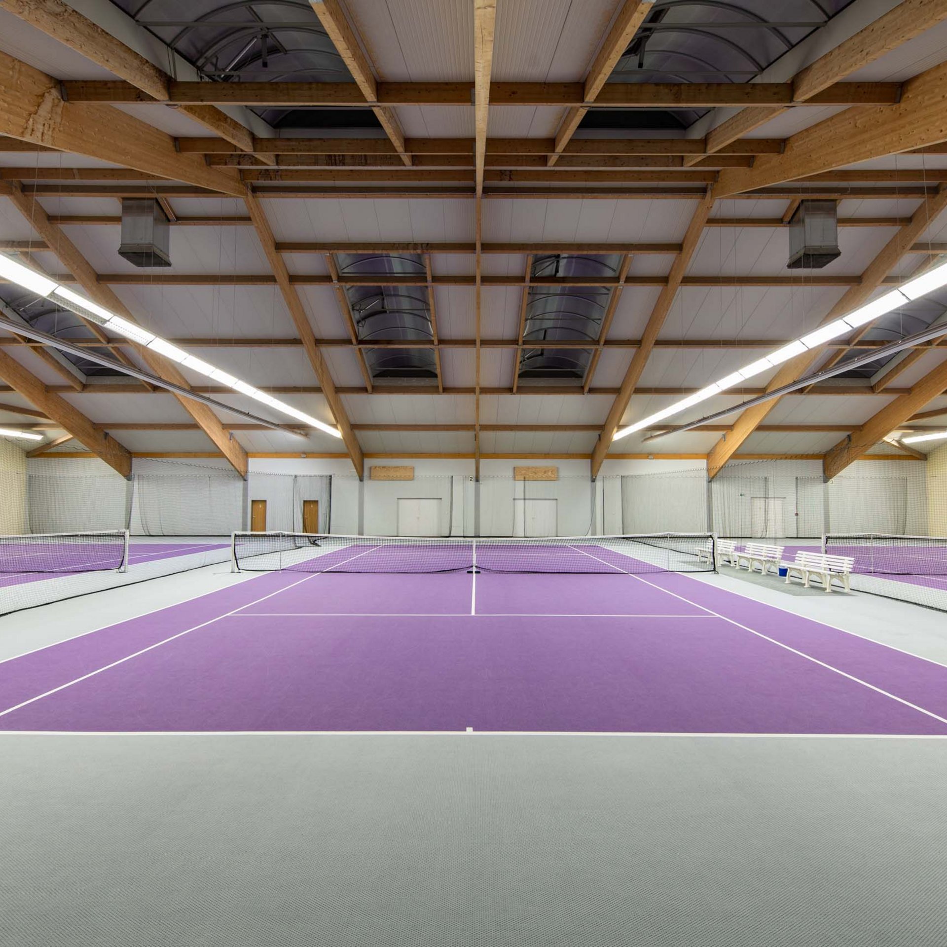 Leerer Hallen-Tennisplatz mit lila Bodenbelag und Holzbalkendecke