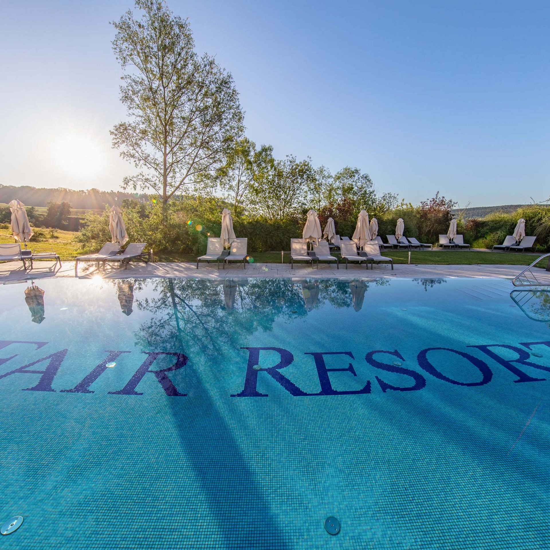 Pool mit FAIR RESORT-Schrift im Wasser bei Sonnenuntergang und Liegestühlen