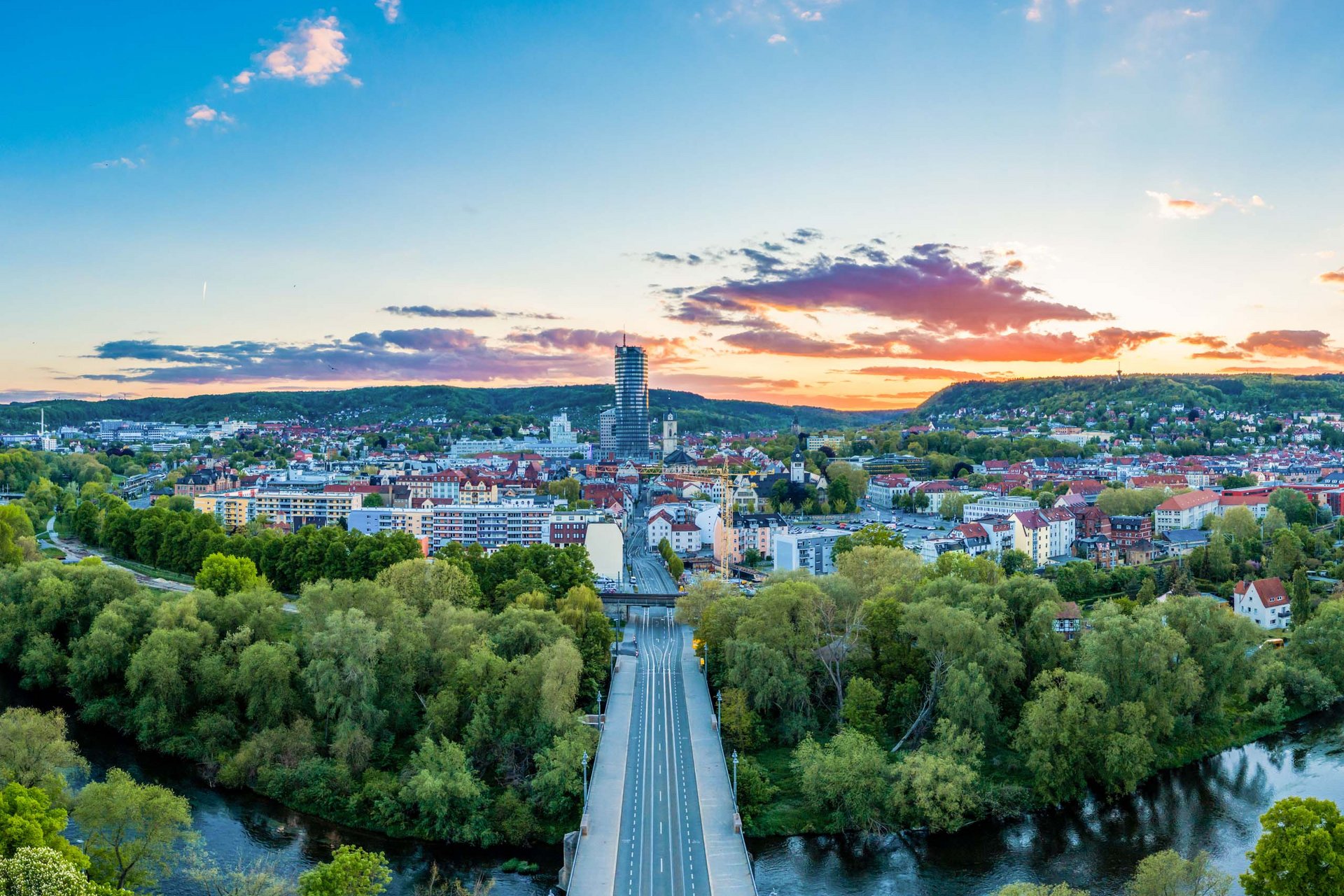 Stadtansicht bei Sonnenuntergang mit Fluss, grünen Bäumen und Hochhaus