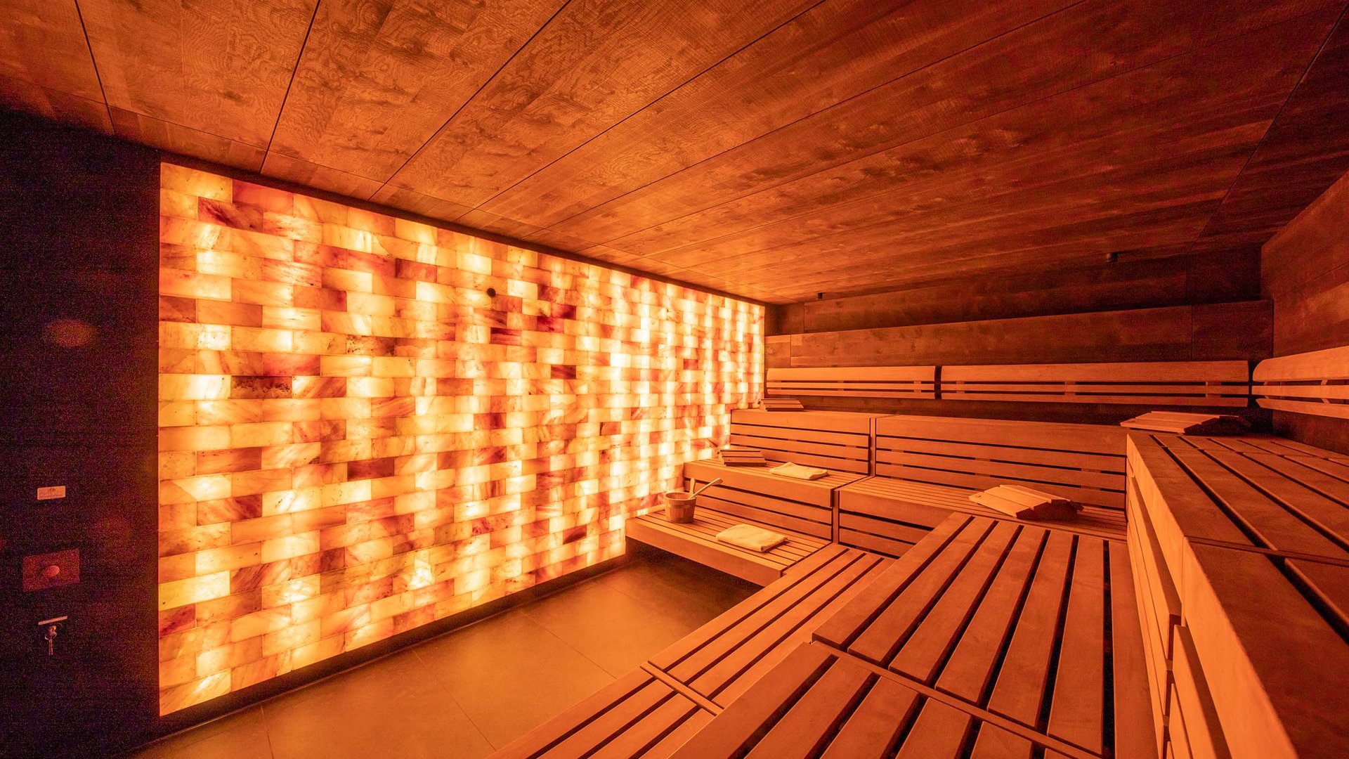 Inside view of a modern sauna with wooden benches and illuminated salt brick wall