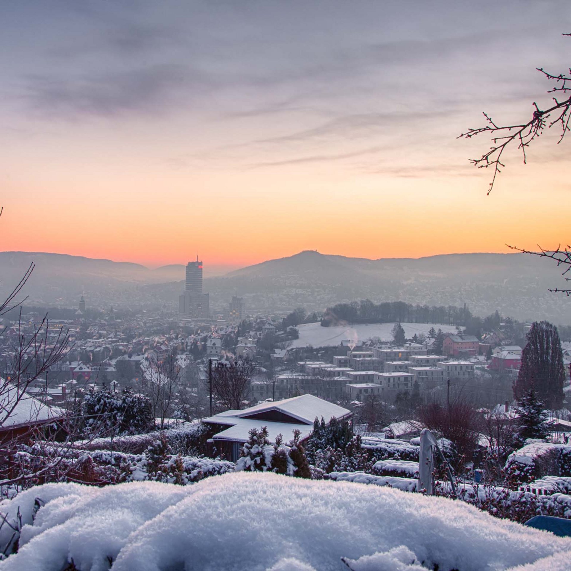 Snow-covered houses and trees at sunset with mountains in the background