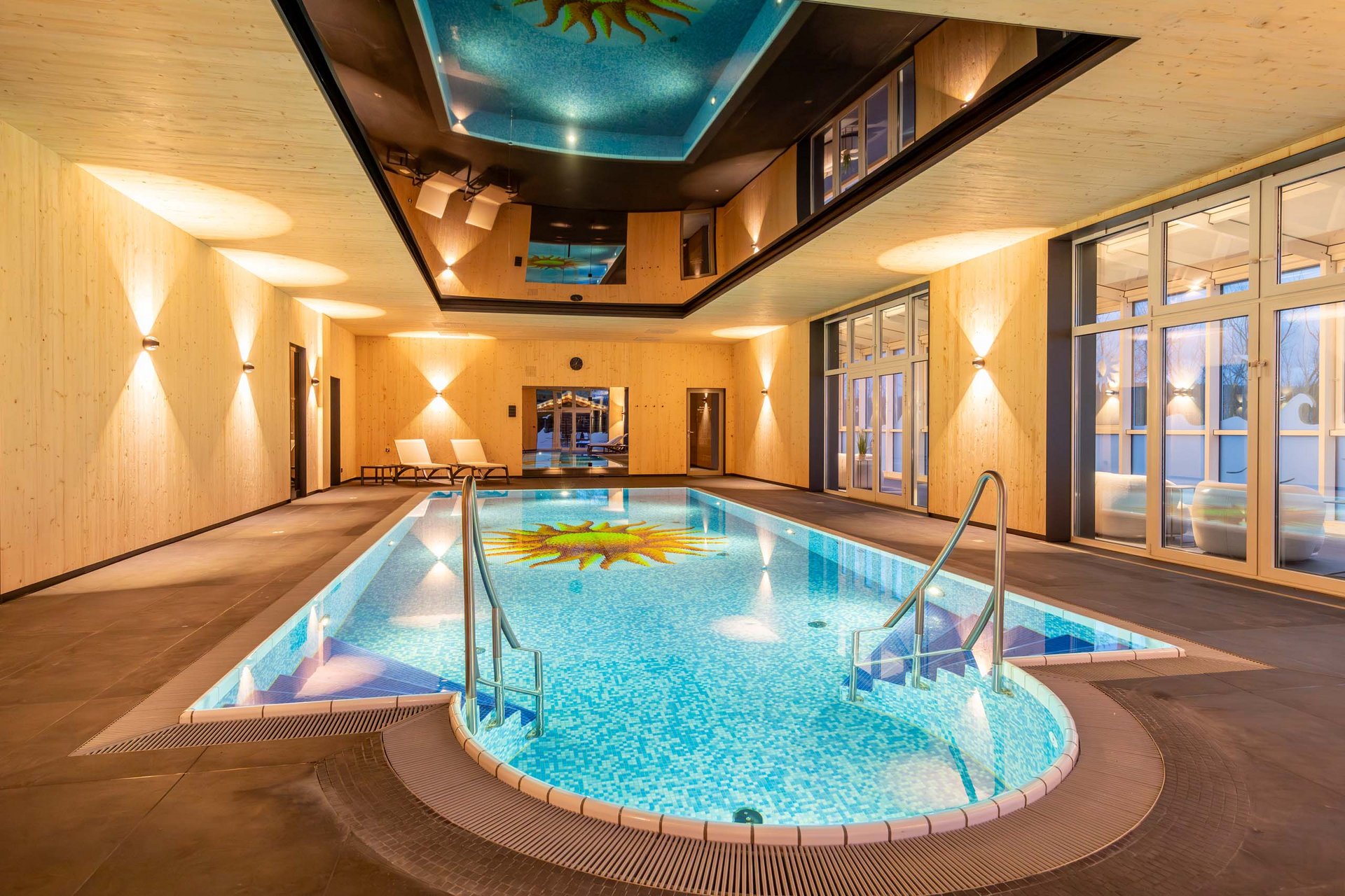 Innenansicht eines modernen Hallenbads mit Holzverkleidung und Sonnendesign im Becken