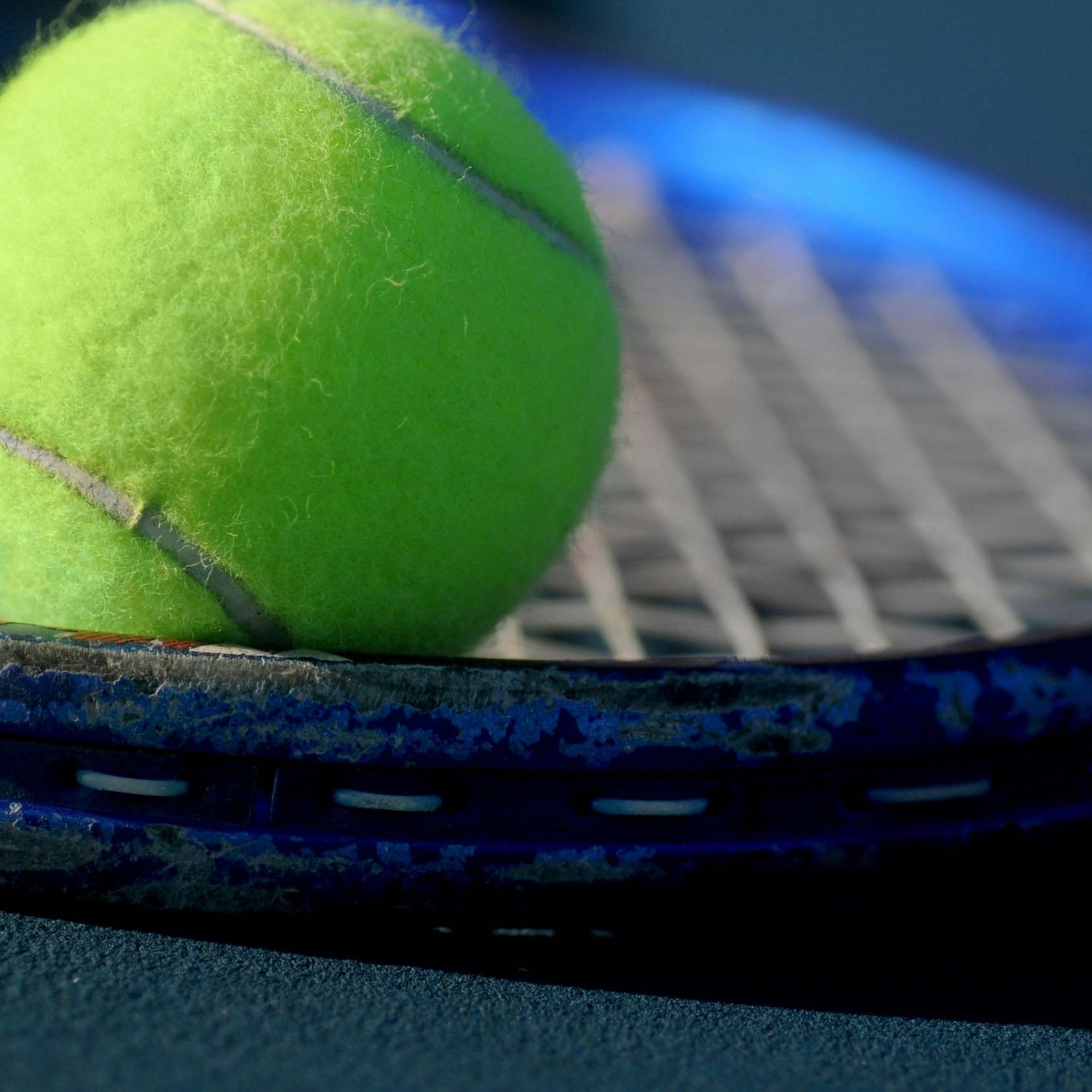Nahaufnahme eines gelben Tennisballs auf einem blauen Tennisschläger