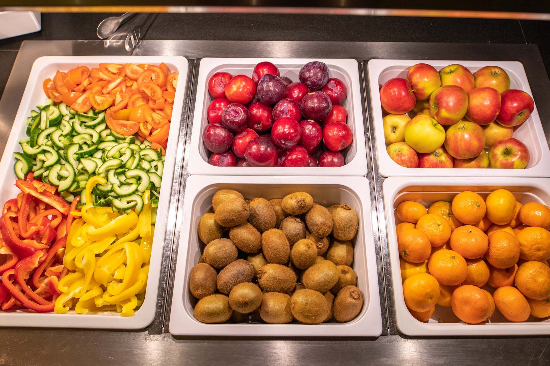 Frisches Obst und geschnittenes Gemüse in weißen Behältern auf einem Buffet