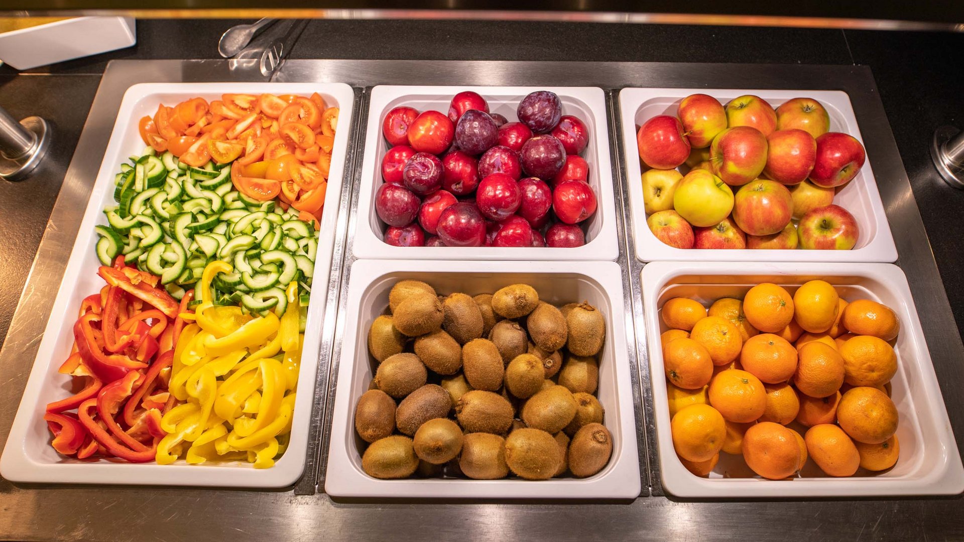 Fresh fruit and sliced vegetables in white containers on a buffet