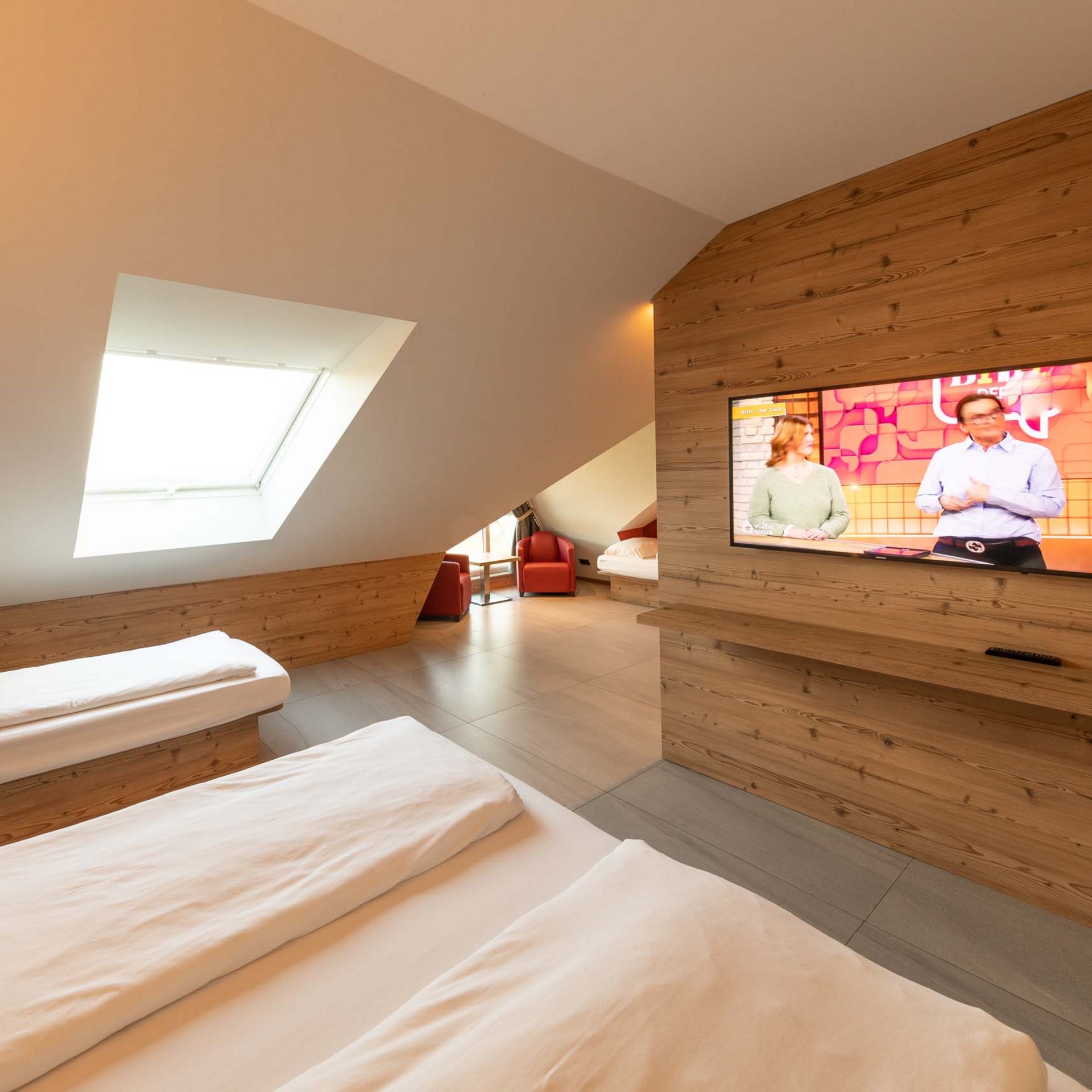 Modern hotel room with two beds, skylight, and TV mounted on wooden panel wall