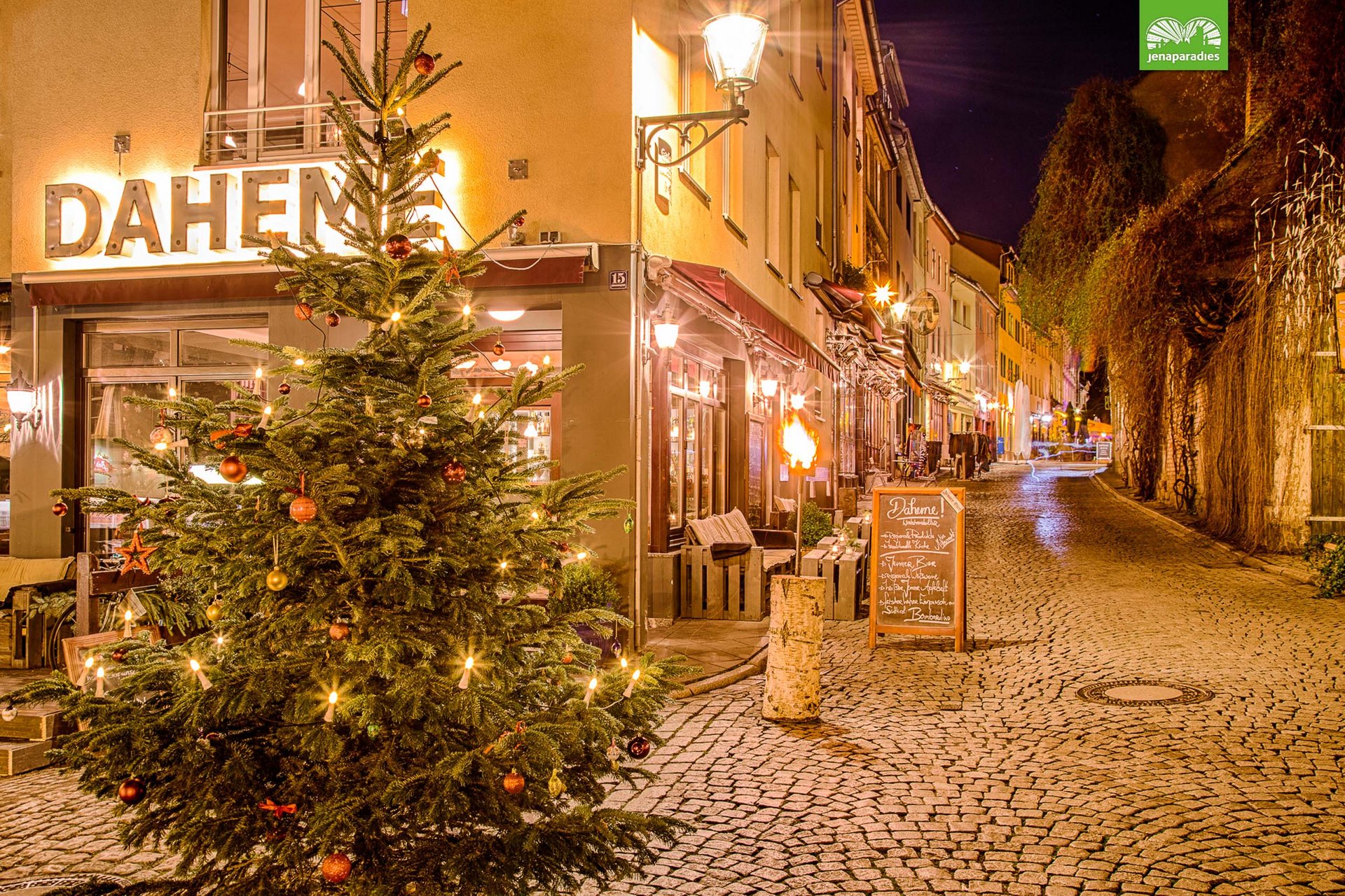 Christmas tree outside lit Daheme restaurant on a quiet cobblestone street at night