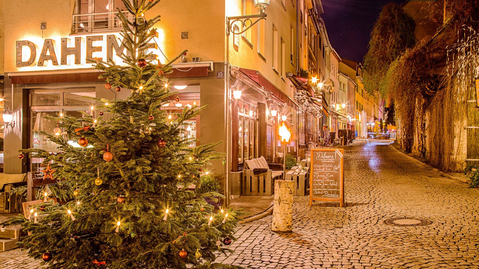 Christmas tree outside lit Daheme restaurant on a quiet cobblestone street at night