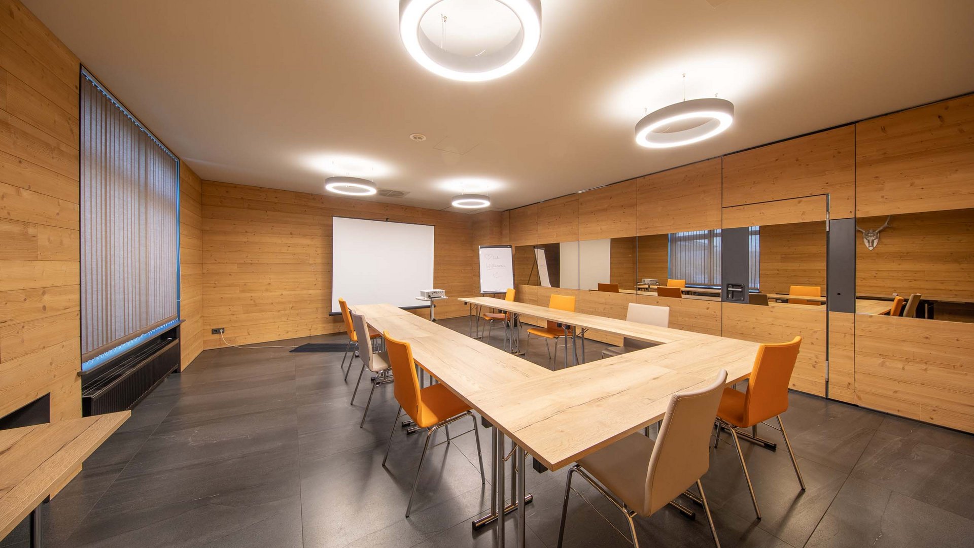 Modern meeting room with wooden walls, U-shaped tables, and orange chairs