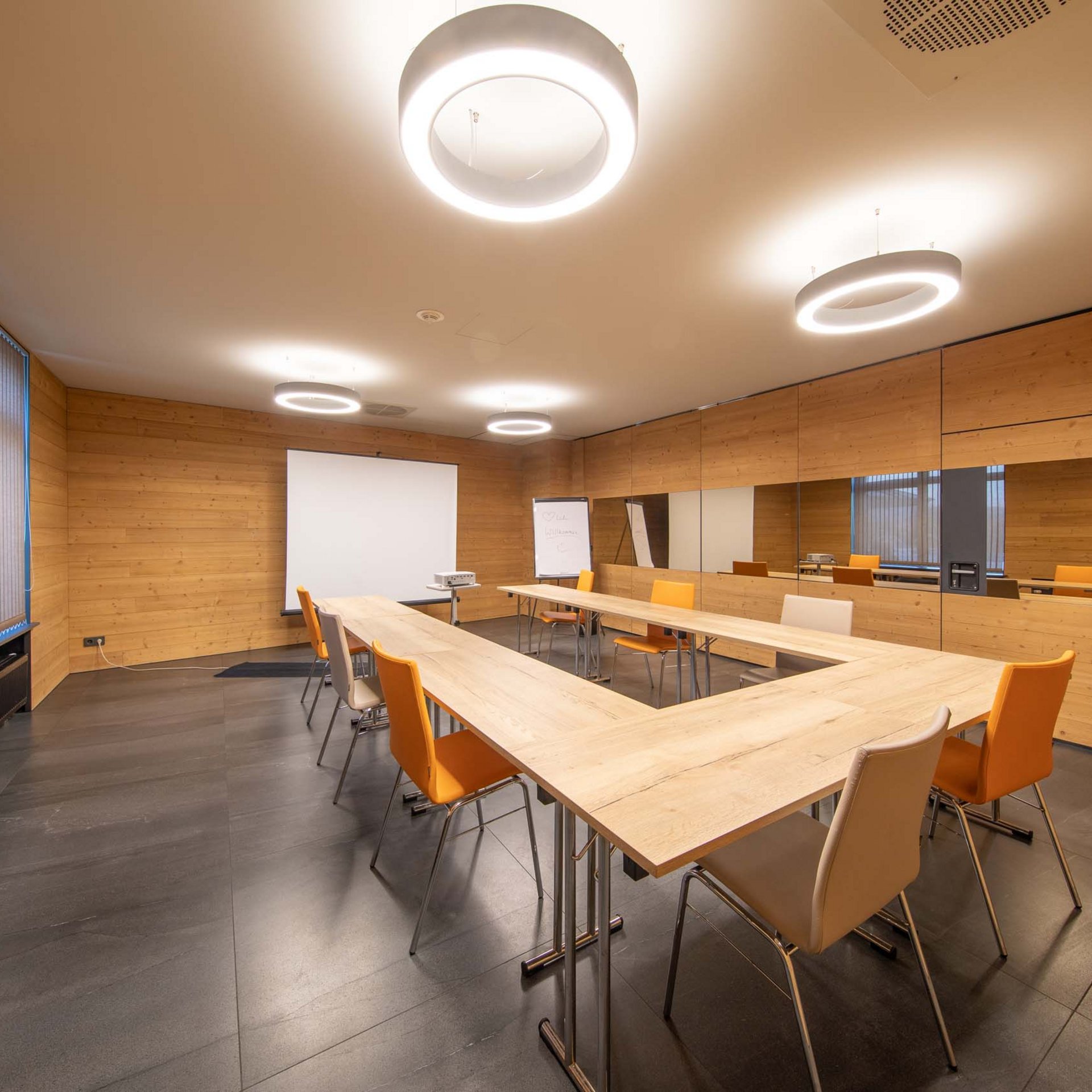 Modern meeting room with wooden walls, U-shaped tables, and orange chairs
